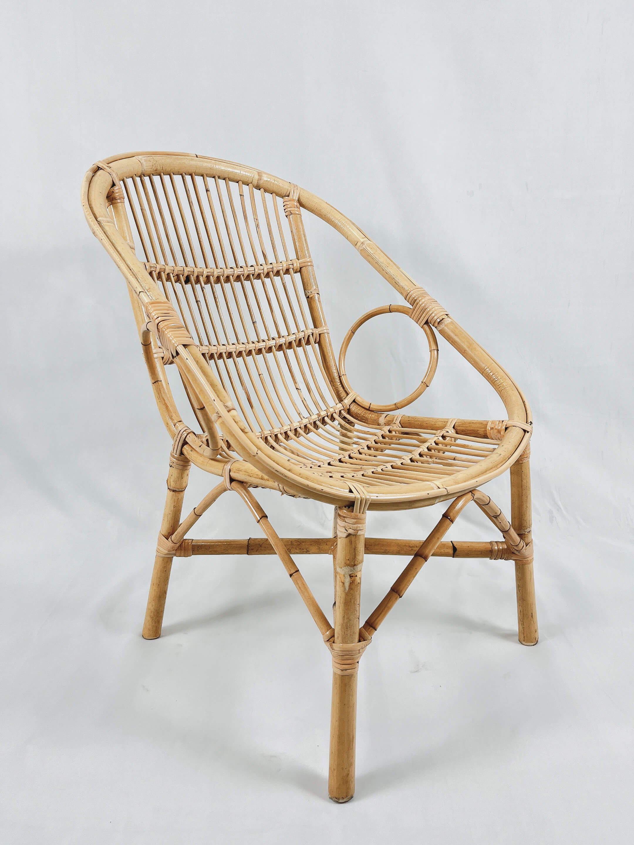 The Two Ring Chair, featuring a bamboo rattan design with a curved backrest and circular accent, is placed against a plain, light-colored background.