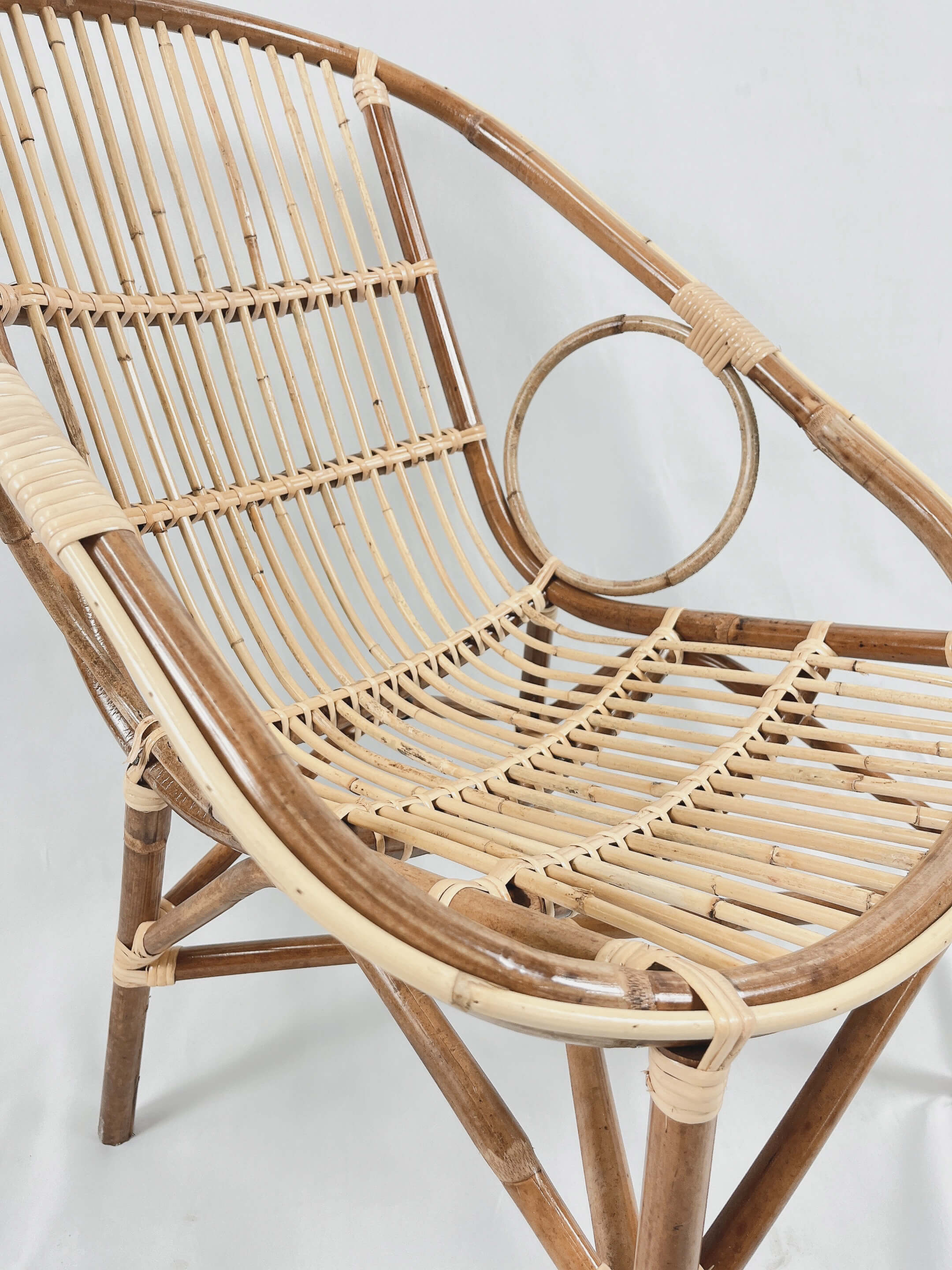 A close-up view of the Two Ring Chair, showcasing its woven wooden rattan seat and backrest, complemented by a distinctive circular design element on the right armrest.