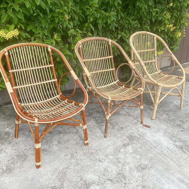 Three Two Ring Chairs of varying shades are arranged on a concrete surface in front of green foliage.