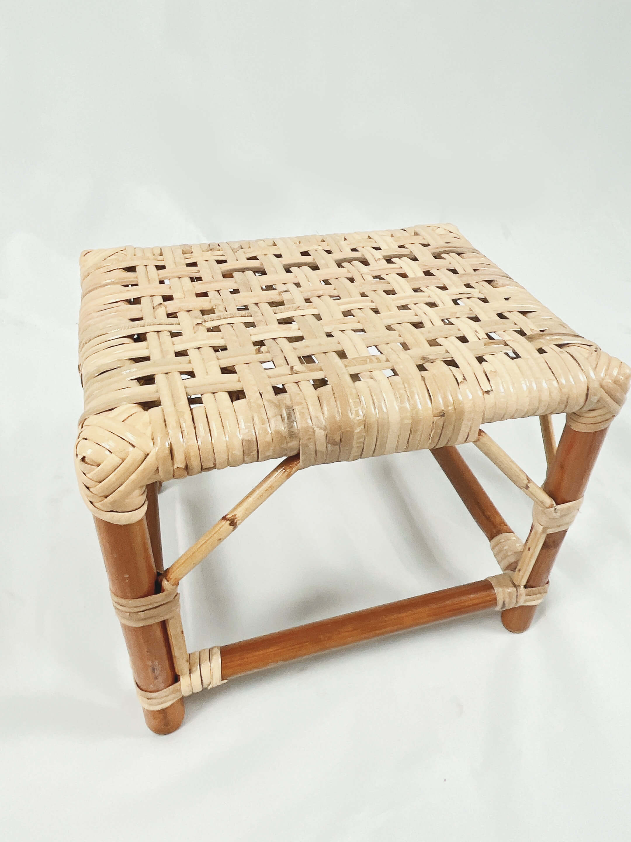 A small, square stool with a woven straw seat and wooden legs.