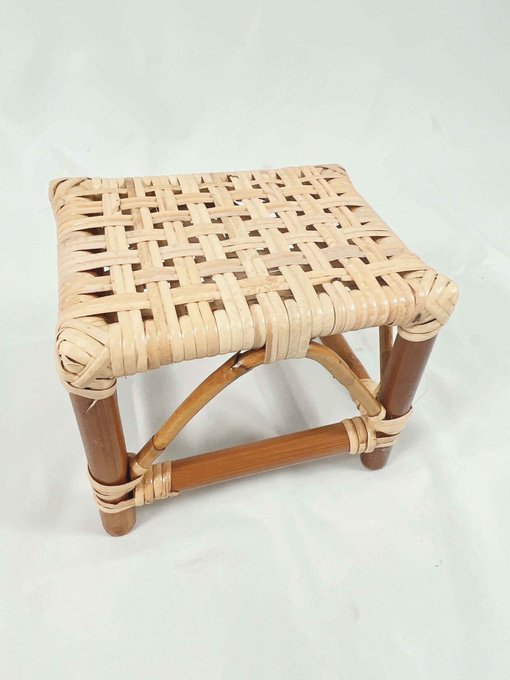 A woven rattan stool with a square seat and wooden legs set against a plain white background.