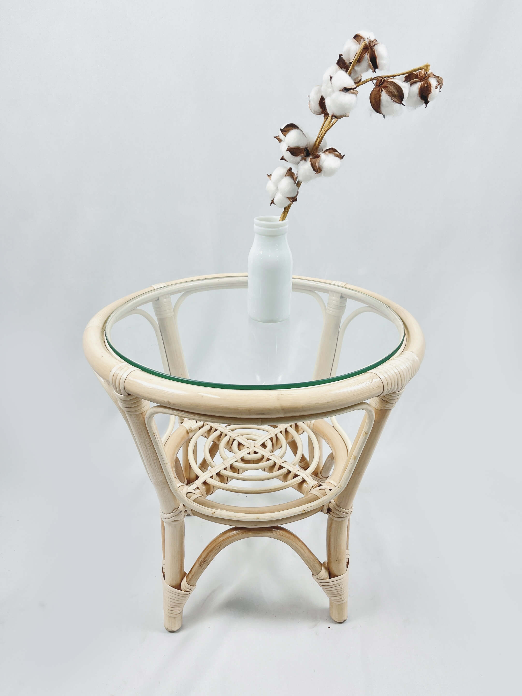 A RC Rattan Table With Glass Top accompanied by a white ceramic vase holding a branch of cotton flowers, photographed against a plain white background.