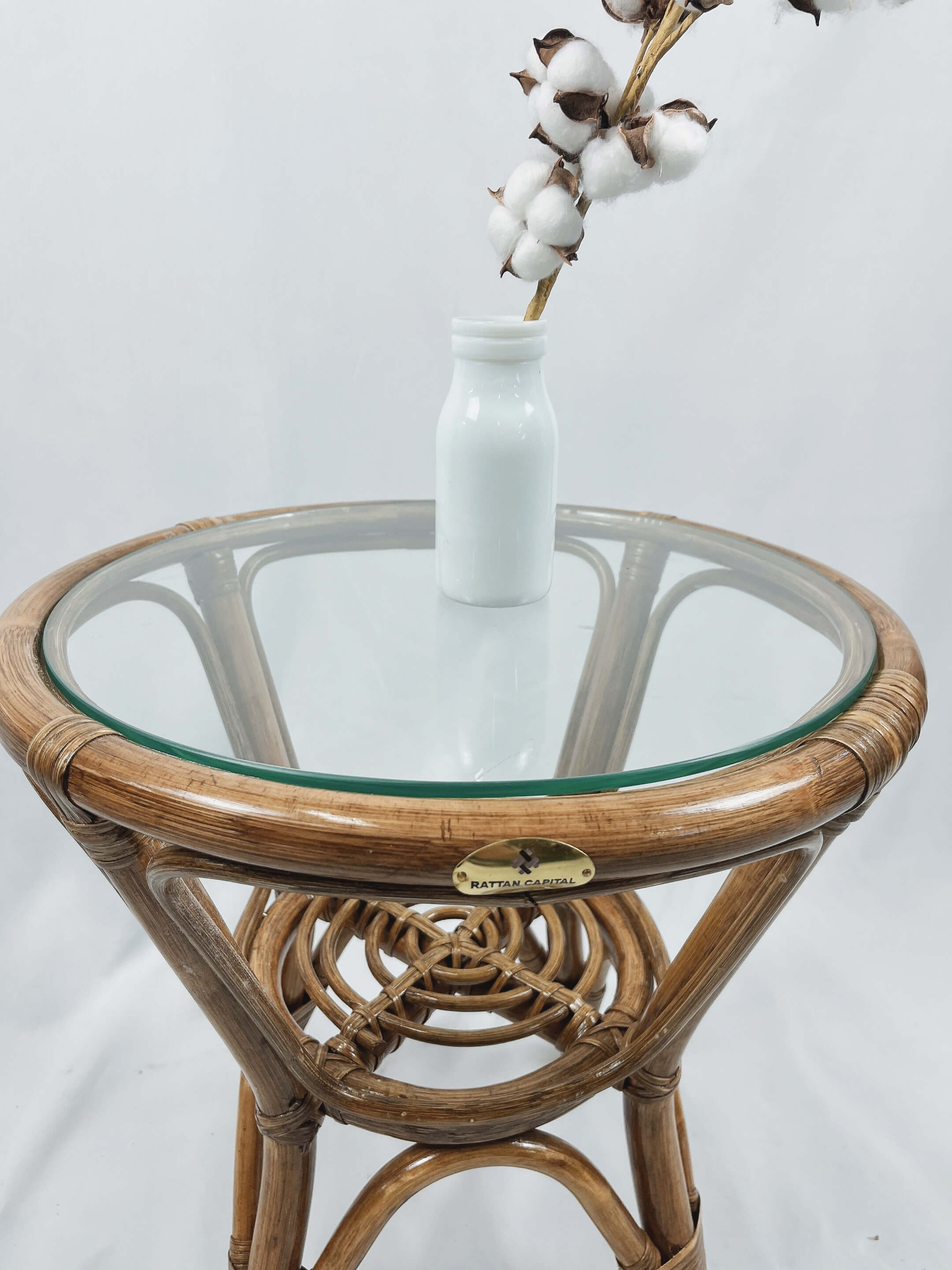 A RC Rattan Table With Glass Top featuring a white vase containing cotton stems placed on top.