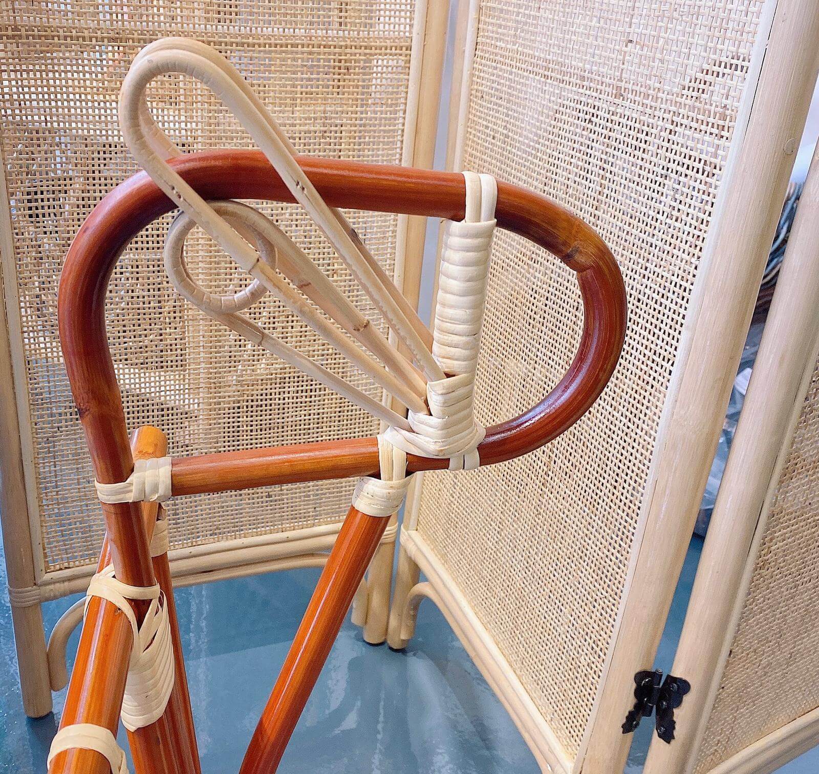 Close-up of the Horse Rocker V2 Webbing with a wooden frame featuring curved edges and white woven bindings. A wicker screen is visible in the background.