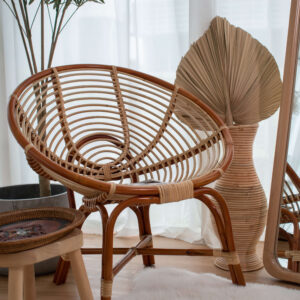 An NN Coil Hami Chair 27" is positioned by a large vase containing a dried fan palm leaf. Nearby, a round wooden side table holds a tray. The scene is accented with a large mirror and potted plant in the background.