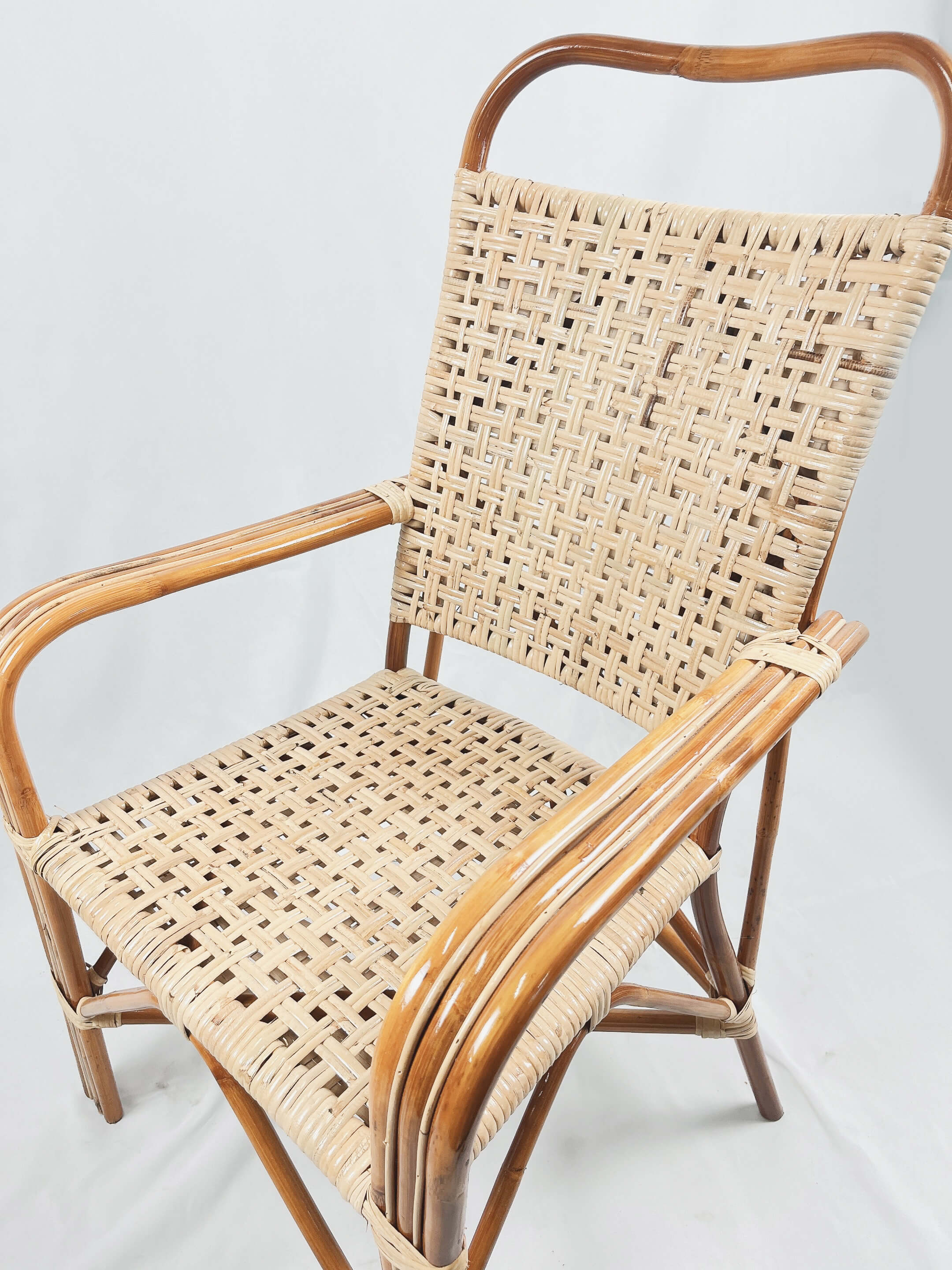 The RC World Chair, featuring a wooden frame with a woven rattan design, armrests, and a high backrest, is set against a plain white background.