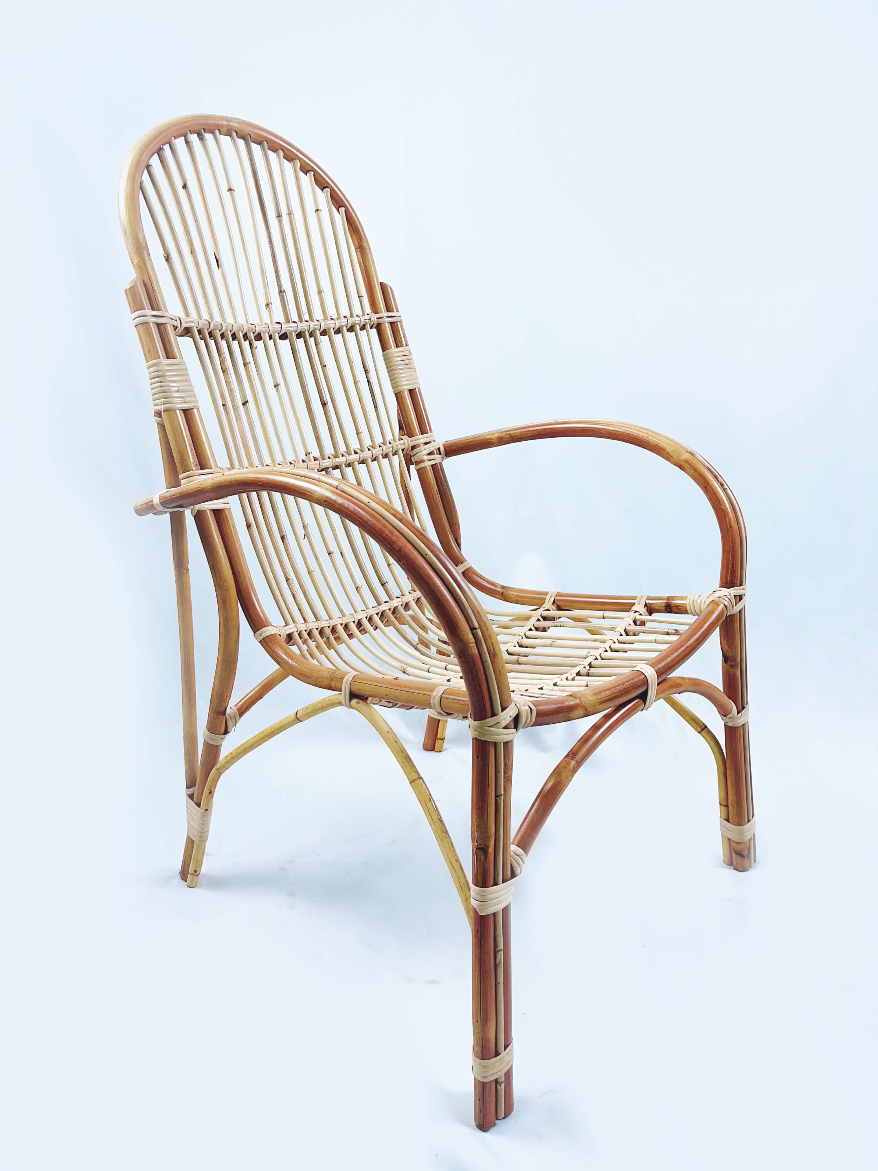 A bamboo chair with a curved backrest and armrests, featuring a woven seat and vertical slats, against a plain white background.