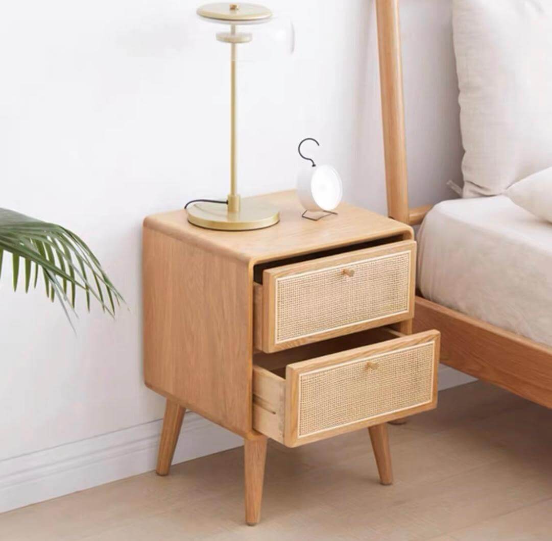 A Raffles Side Table with two open drawers, a gold lamp, and a small white clock beside a bed in a minimalist bedroom.