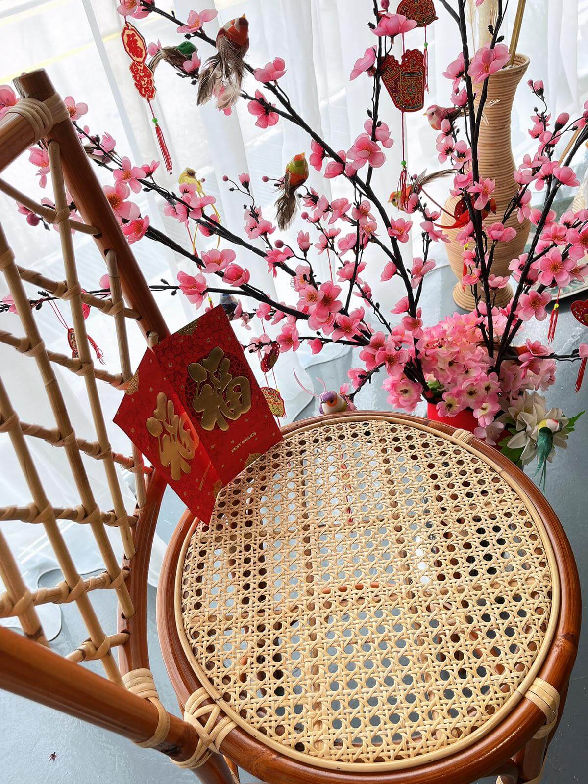 A PO - RC Bar Stool (With Backframe) sits against a backdrop of pink cherry blossom branches adorned with red envelopes and decorations.
