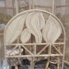 The Artistic Natural Leaf Rattan Single Headboard (Clearance) with leaf patterns is displayed in front of a wicker room divider, beside a small log stool and a bamboo stool.