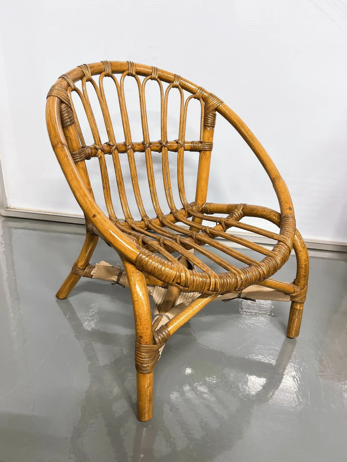 A wooden rattan chair with a round backrest and woven seat is placed on a smooth, gray floor against a white wall.