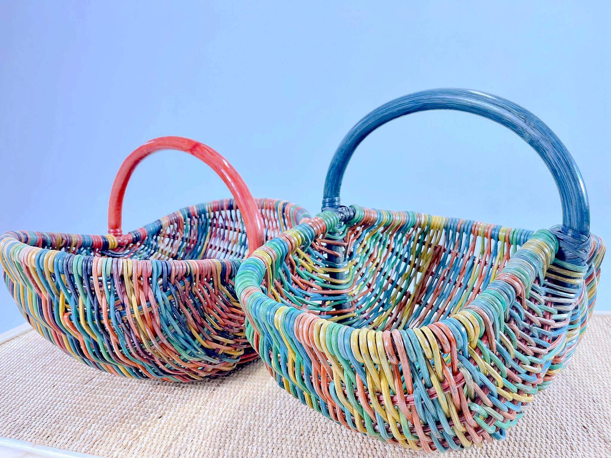 Two Wicker Basket LK10s, featuring vibrant, multicolored patterns and handles in red and blue, are placed on a beige surface against a light blue background.