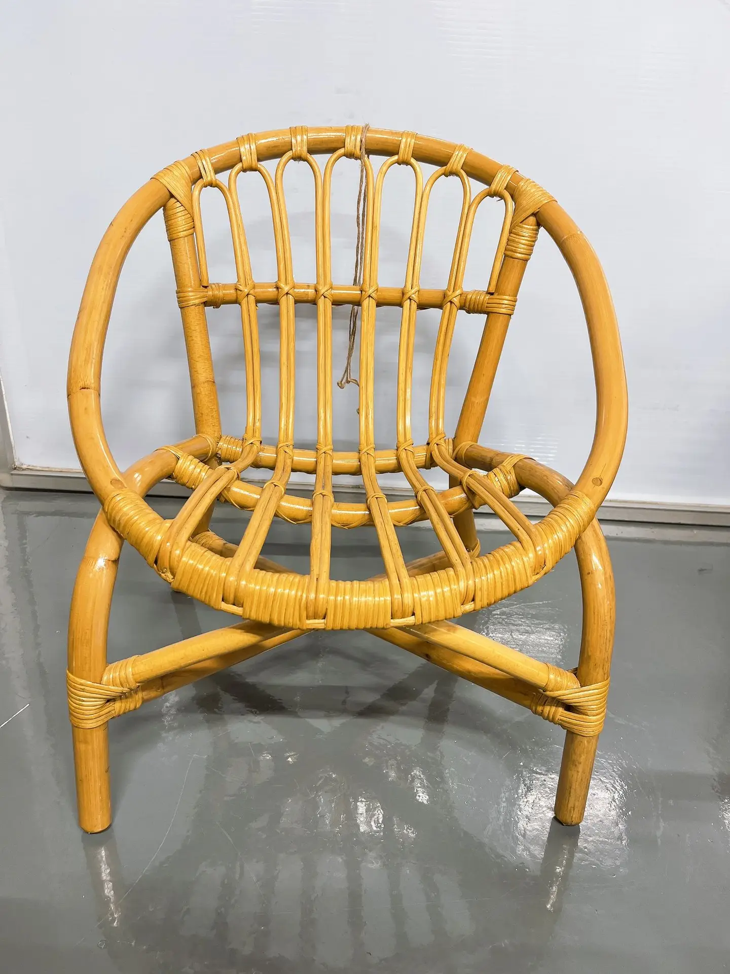 A rattan chair with a curved backrest and seat made of woven rattan material, placed on a gray floor with a white background.