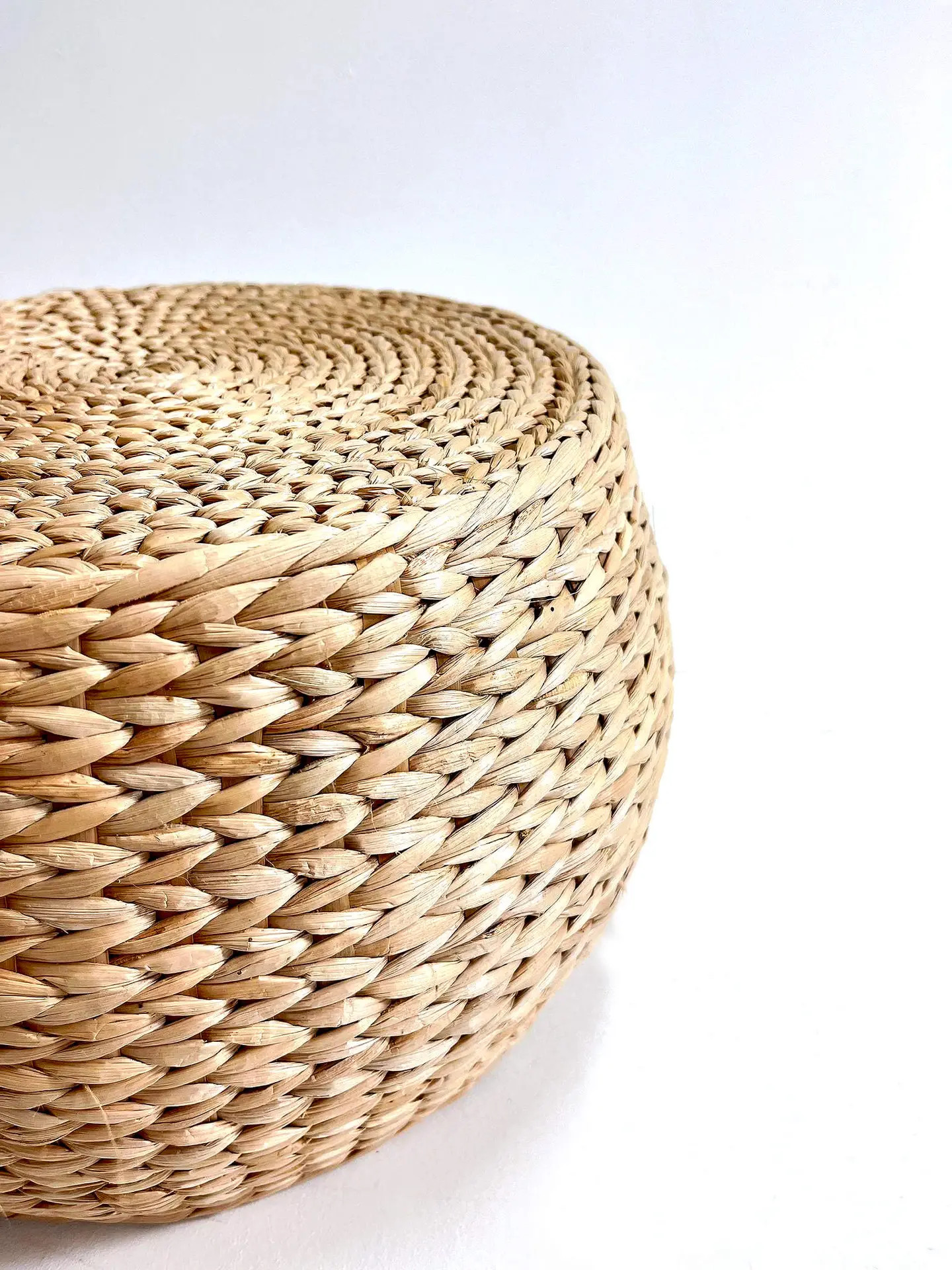 A close-up of a Seagrass Ottoman with a flat, circular top placed against a white background.