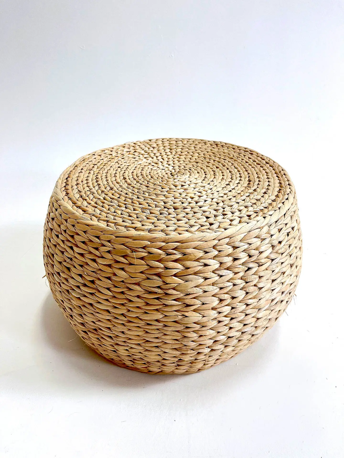 A round, woven natural-fiber ottoman with a tightly braided design sits against a plain white background.