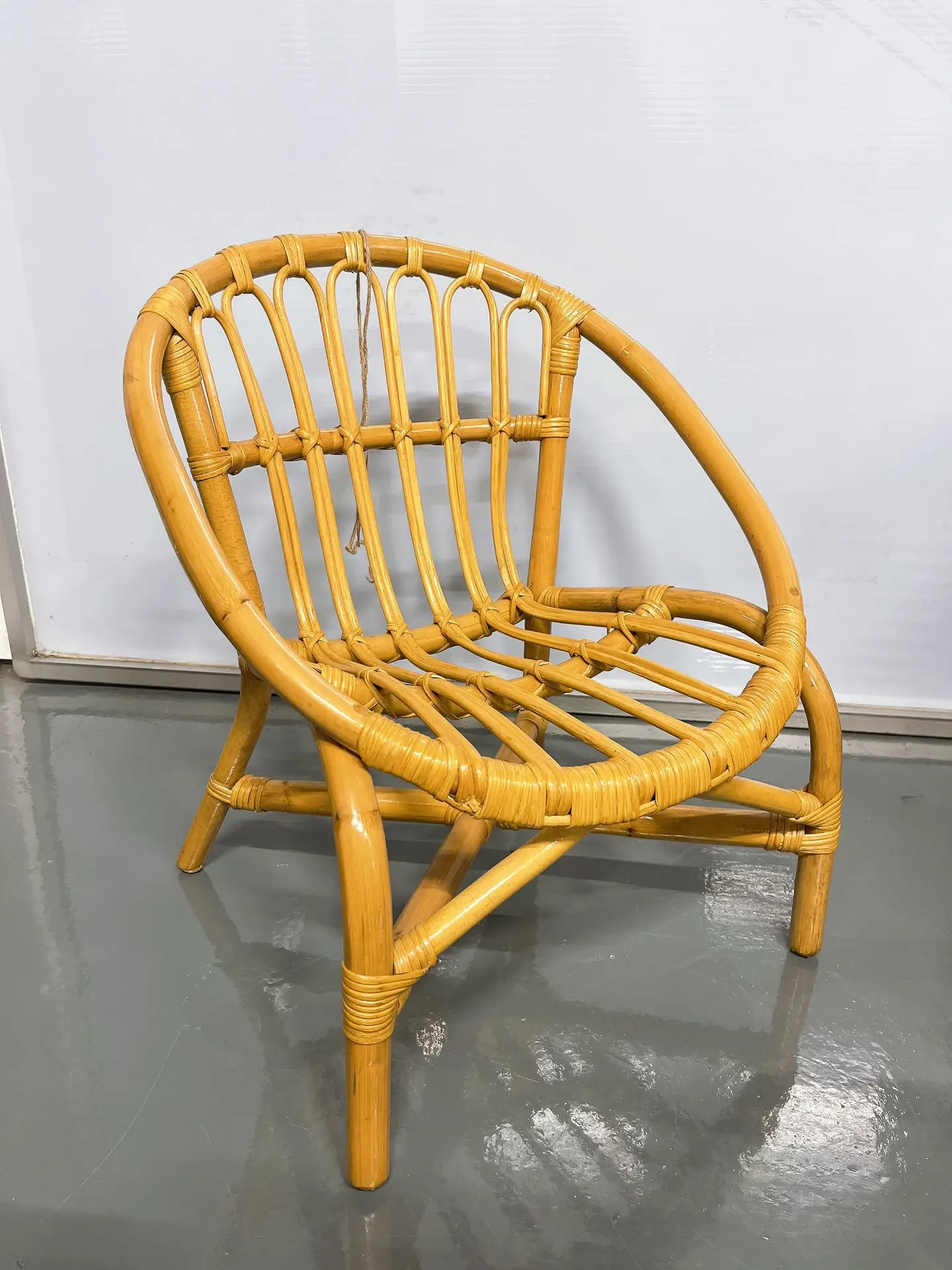 A bamboo chair with a curved backrest and seat, featuring a woven design and four legs, placed on a gray floor against a white background.