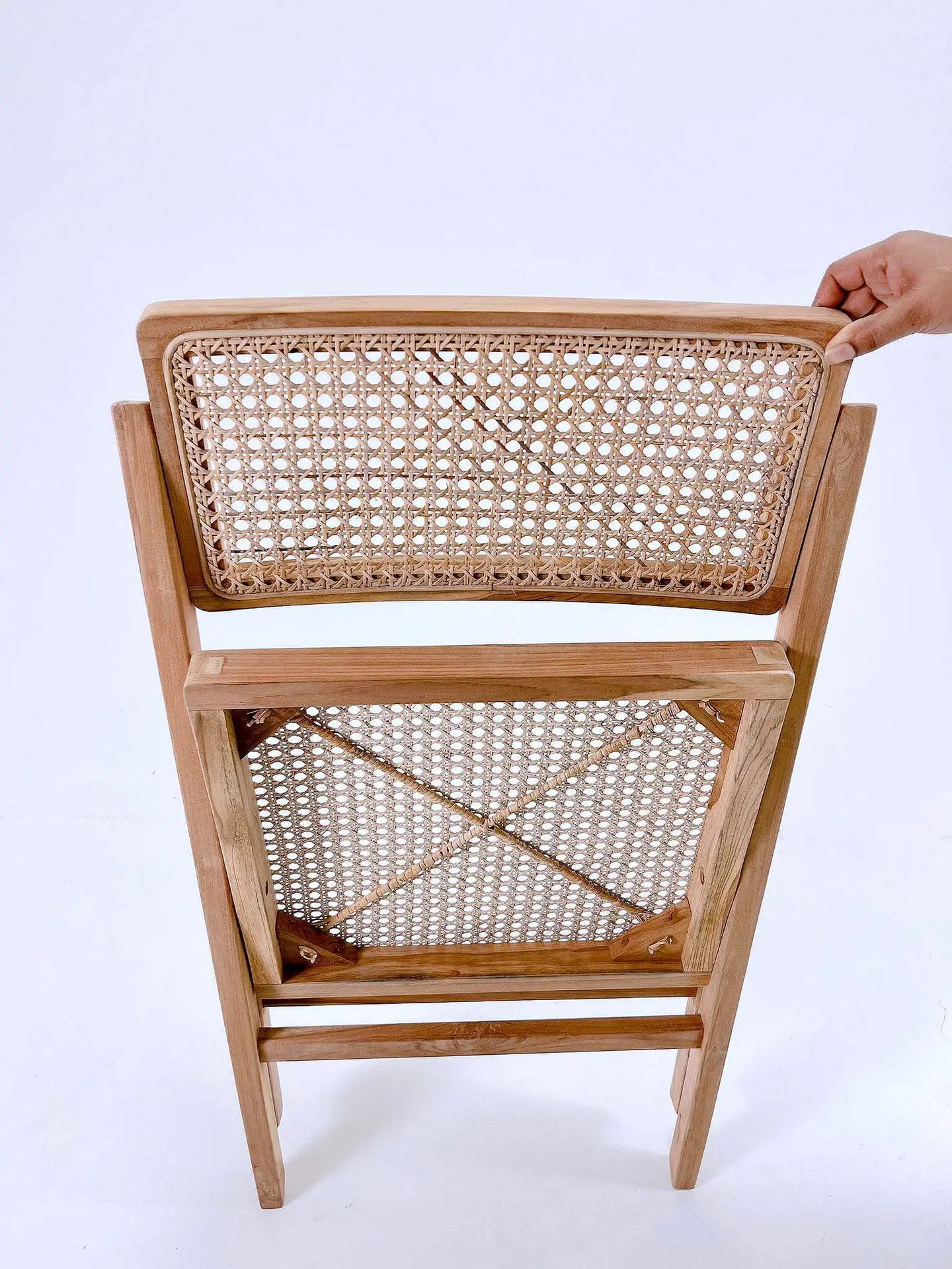 A wooden folding chair is shown from the back with a hand holding the top edge. The backrest and seat feature a woven wicker pattern.