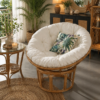 The Manau Papasan With Natural Frame and cushion features a round rattan design with a white cushion, perfect for cozy, plant-filled living spaces with wicker furniture and natural decor.