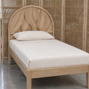 A single bed featuring the Artistic Natural Leaf Rattan Single Headboard (Clearance) with beige bedding stands on a concrete floor, set before a woven rattan room divider.