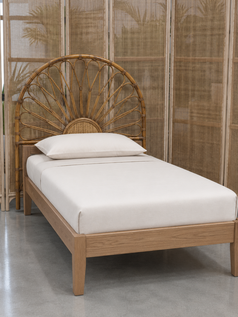 A single bed featuring the Floral Natural Rattan Headboard (Clearance) and a light wood frame is positioned in front of a woven room divider on a polished concrete floor.