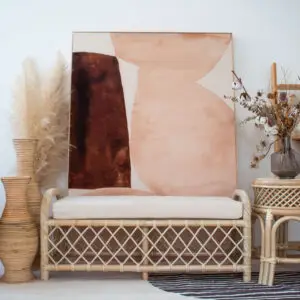 A minimalist living space features a Twister Bench, two large woven vases, a small side table with dried flowers, and abstract artwork leaning against the wall.