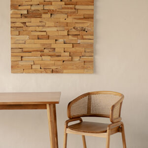 A wooden table and chair are placed in front of a beige wall with a decorative wooden panel hanging above.