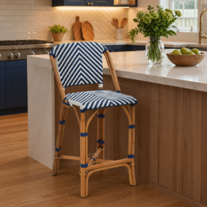 A French Cafe Bar Stool (Clearance) with a blue and white woven seat and bamboo frame is placed by a marble kitchen island decorated with a vase of flowers and a bowl of green apples.