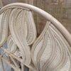 Close-up of the Artistic Natural Leaf Rattan Single Headboard (Clearance), showcasing its curved, leaf-inspired woven backrest in light wood tones, positioned before a coordinating rattan room divider.