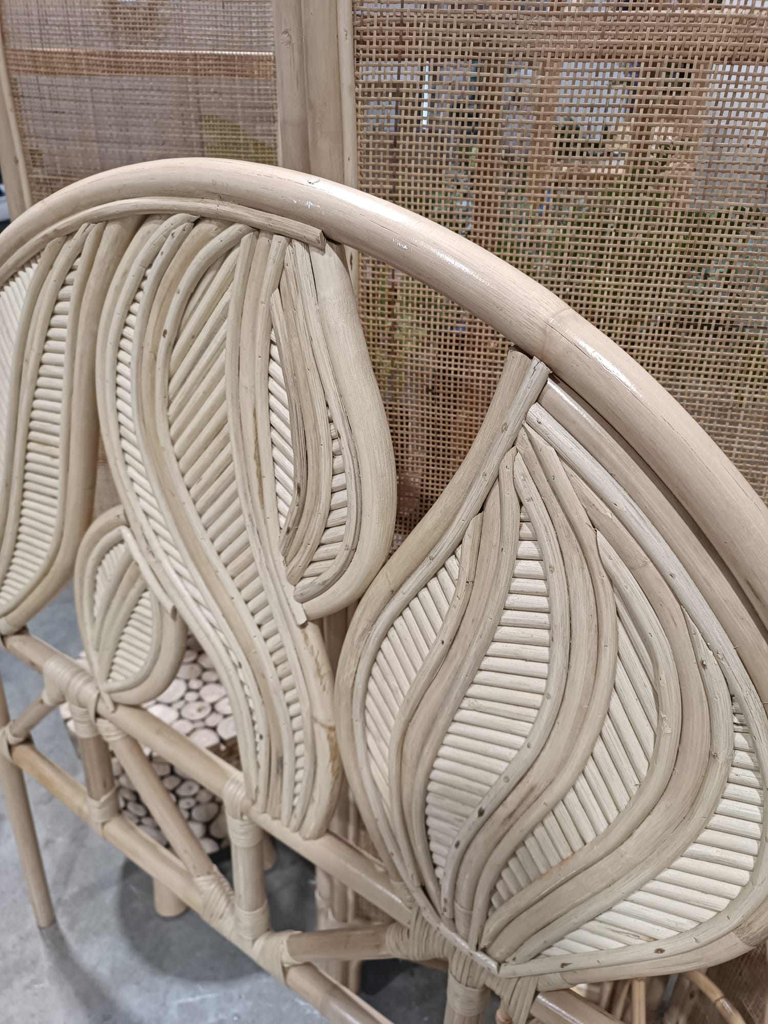 Close-up of the Artistic Natural Leaf Rattan Single Headboard (Clearance), showcasing its curved, leaf-inspired woven backrest in light wood tones, positioned before a coordinating rattan room divider.