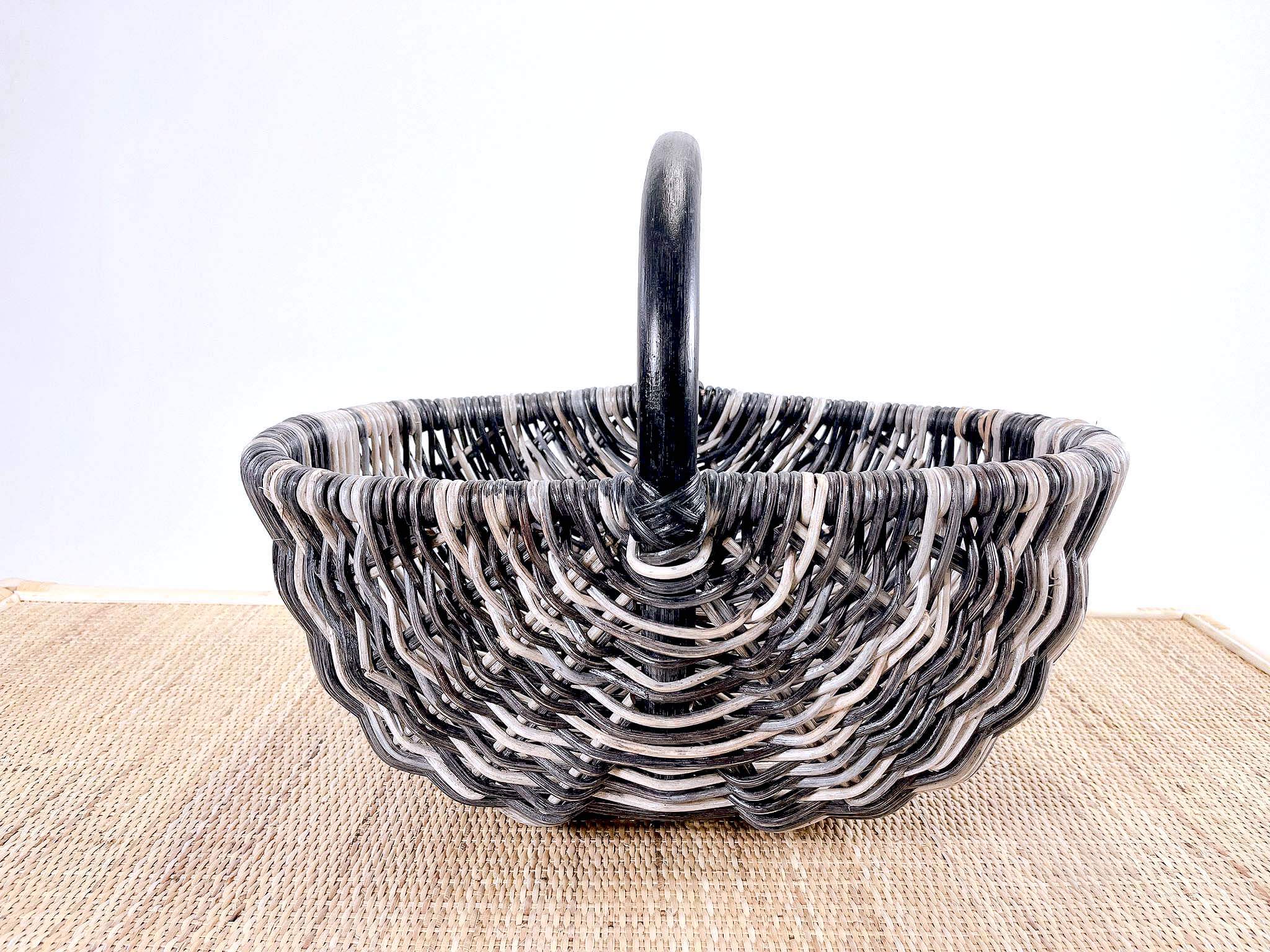The Wicker Basket LK10, characterized by its round shape and black and white woven design with a handle, is placed on a textured surface.