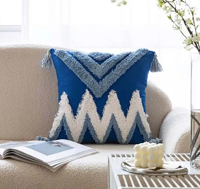 Abstract textured embroidery cushion cover adorns a cream sofa, complemented by an open book and a decorative candle on the nearby table.