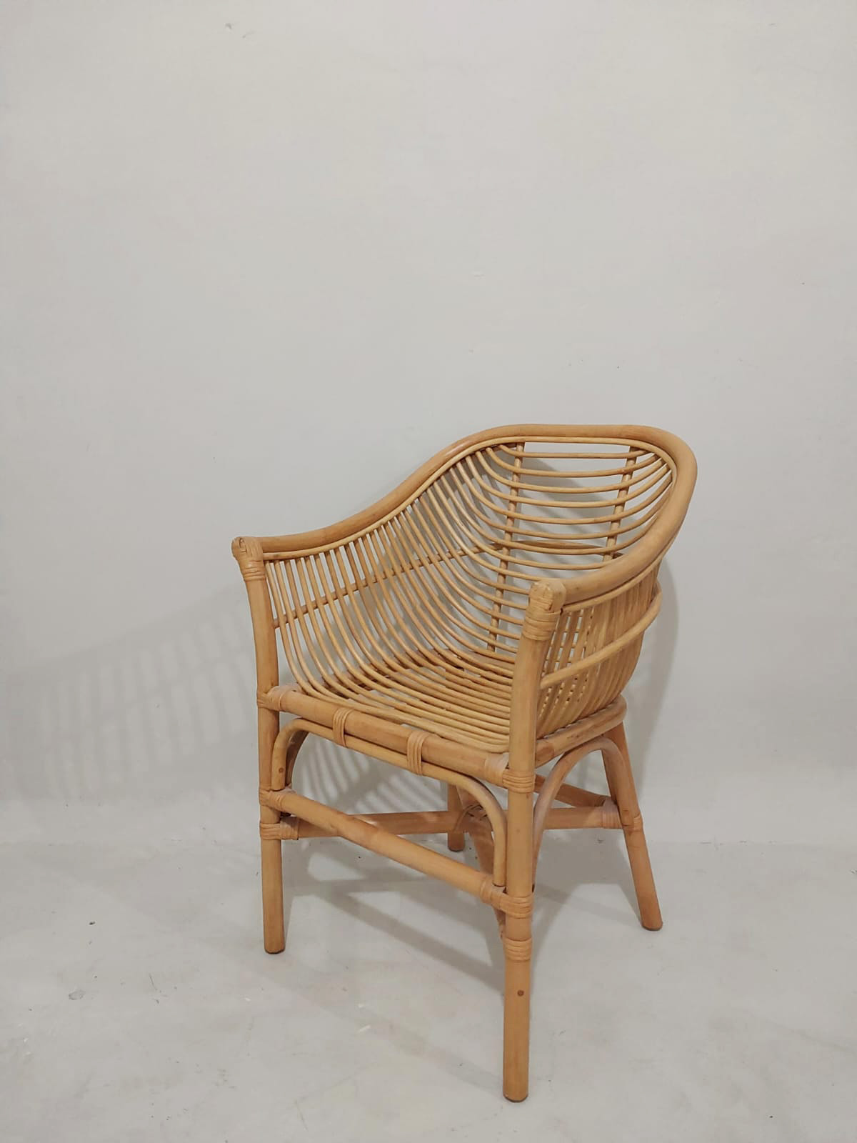 The Lazio Core Chair, featuring curved armrests, a woven backrest and seat, and a white seat cushion, sits on a light-colored floor against a white wall.