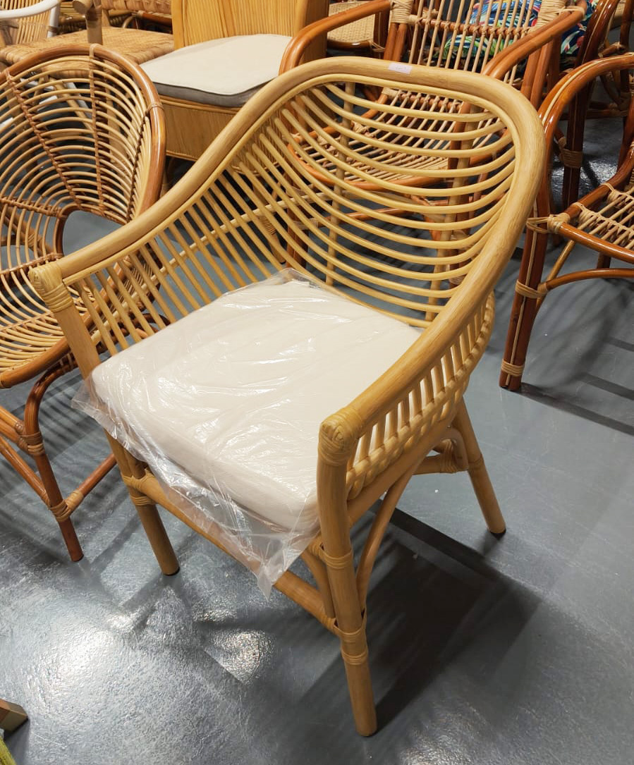 The Lazio Core Chair, featuring a curved rattan back and armrests, comes with a white seat cushion and is shown on a gray floor among similar chairs.