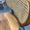A close-up of the Moni Chair showcasing its wooden frame, woven cane backrest, and polished wooden seat, set against a gray floor.