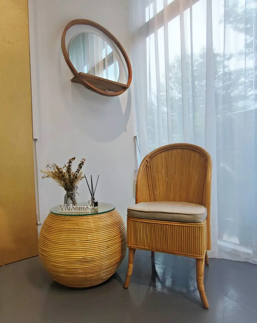 A Zera Chair (New Arrival) and a matching side table with a vase of dried flowers are placed next to a sheer curtained window. Above them hangs a circular mirror with a wooden frame.