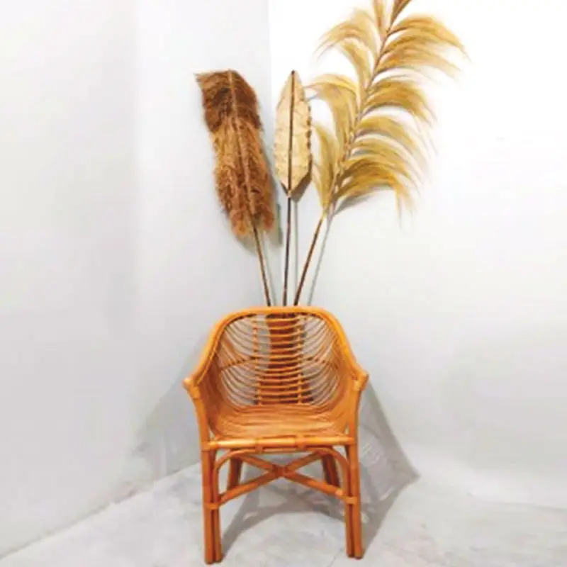 A Lazio Core Chair is placed in a corner with tall dried pampas grass and decorative stalks behind it against a plain white wall.