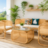 A sunlit balcony features the Zorba Sofa Set (Clearance) with rattan design, a glass-top coffee table, potted plants, decorative pillows, and a shelf with small decor against a white wall.