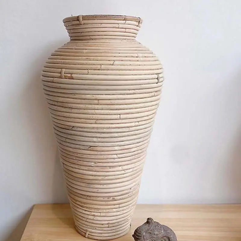 A large, ribbed ceramic vase with a narrow neck sits on a wooden surface next to a small, intricately carved stone figurine.