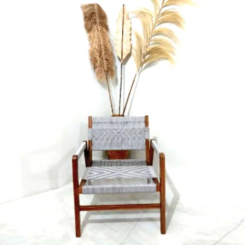 A **Wooden Chair With Rope Grey** positioned in front of tall, wispy dried grasses against a plain white wall.