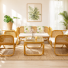 A sunlit living room features the Zorba Sofa Set with white cushions, a wicker rug, tropical plants, and a framed botanical print. A small table holds drinks and a flower vase.