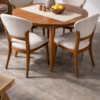 A round wooden dining table with four upholstered chairs, a beige runner, a bowl of lemons, and a vase with dried flowers on top, set on a polished concrete floor. A round wooden dining table with four upholstered chairs, a beige runner, a bowl of lemons, and a vase with dried flowers on top, set on a polished concrete floor.